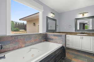Full bath featuring a jetted tub, vanity, stone tile floors, and a mountain view