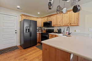 Kitchen with black appliances, light wood-type flooring, a peninsula, light brown cabinets, and light stone countertops