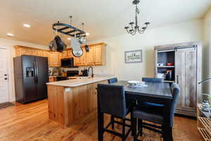 Kitchen featuring black appliances, a peninsula, light wood finished floors, light countertops, and a textured ceiling