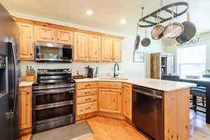 Kitchen featuring appliances with stainless steel finishes, light brown cabinetry, a peninsula, light wood-style flooring, and light countertops