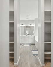 Full bathroom featuring wood finished floors, double vanity, a walk in closet, and built in shelves