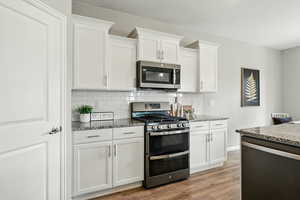 Kitchen featuring stainless steel appliances, stone countertops, tasteful backsplash, and light wood-style flooring
