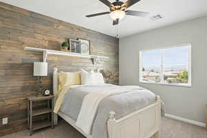 Bedroom with carpet, wooden walls, and a ceiling fan