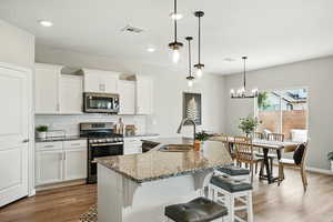 Kitchen featuring stainless steel appliances, wood finished floors, stone counters, decorative backsplash, and white cabinetry