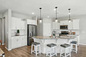Kitchen featuring stainless steel appliances, backsplash, dark wood finished floors, white cabinets, and a breakfast bar