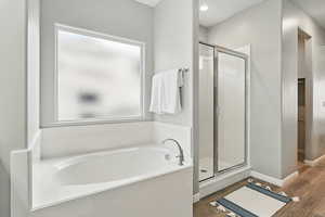 Full bathroom featuring a stall shower, a bath, and wood finished floors