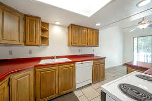 Kitchen with white dishwasher, range, brown cabinetry, light tile patterned floors, and recessed lighting