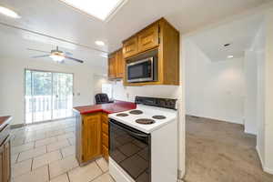 Kitchen with electric range, stainless steel microwave, brown cabinetry, a peninsula, and a ceiling fan
