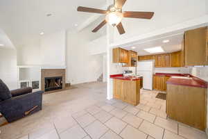 Kitchen with white appliances, light tile patterned floors, light carpet, ceiling fan, and a fireplace
