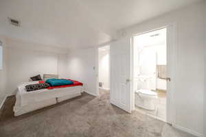 Carpeted bedroom featuring ensuite bath and baseboards