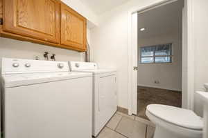 Washroom with washing machine and clothes dryer, light colored carpet, light tile patterned flooring, and cabinet space