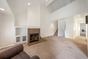Unfurnished living room featuring carpet, a tile fireplace, recessed lighting, stairs, and a high ceiling