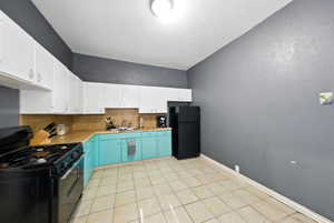 Kitchen with black appliances, decorative backsplash, light countertops, and white cabinetry