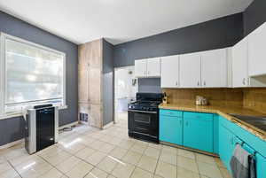 Kitchen with black gas stove, decorative backsplash, white cabinetry, and light tile patterned flooring