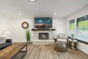 Living room with ornamental molding, a stone fireplace, wood finished floors, and recessed lighting