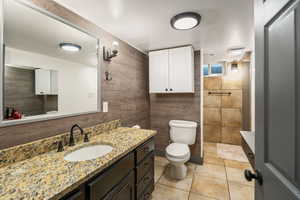 Full bath with vanity, tile patterned floors, tiled shower, and tile walls