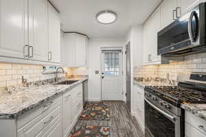 Kitchen with stainless steel appliances, white cabinets, light stone counters, tasteful backsplash, and dark wood-style floors