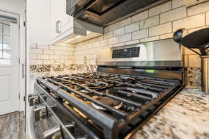 Kitchen view of gas stove, backsplash, white cabinets, and light stone counters