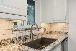 Kitchen with dishwasher, light stone countertops, decorative backsplash, and white cabinets