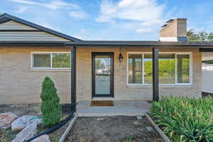 Entrance to property featuring a chimney, brick siding, and covered porch