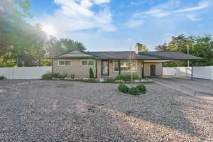 View of front facade with a carport, a gate, concrete driveway, a chimney, and brick siding