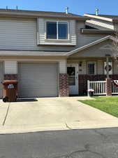 Multi unit property with brick siding, an attached garage, driveway, a shingled roof, and covered porch