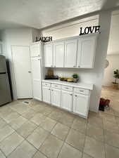 Kitchen featuring freestanding refrigerator, light tile patterned flooring, light countertops, and white cabinetry