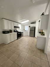 Kitchen featuring stainless steel appliances, light tile patterned floors, under cabinet range hood, light countertops, and white cabinetry