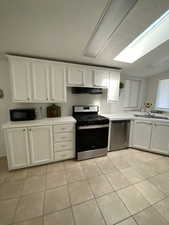 Kitchen featuring stainless steel appliances, under cabinet range hood, light tile patterned floors, light countertops, and white cabinetry