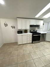 Kitchen with stainless steel appliances, ventilation hood, light tile patterned flooring, and light countertops