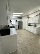 Kitchen featuring freestanding refrigerator, range with gas stovetop, black microwave, light tile patterned floors, and a skylight