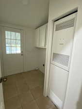 Laundry room with cabinet space, a heating unit, and light tile patterned floors