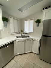 Kitchen featuring appliances with stainless steel finishes, vaulted ceiling, light tile patterned floors, and white cabinetry