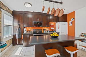 Kitchen featuring appliances with stainless steel finishes, dark countertops, a center island, a breakfast bar area, and a textured ceiling