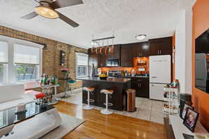 Kitchen with freestanding refrigerator, dark countertops, brick wall, a textured ceiling, and a ceiling fan