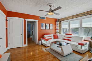 Living room with a ceiling fan, light wood-style floors, and a textured ceiling