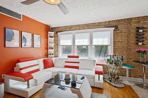 Living room featuring brick wall, ceiling fan, a textured ceiling, and wood finished floors