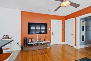 Living room featuring a ceiling fan, wood finished floors, and a textured ceiling