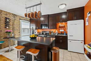 Kitchen with appliances with stainless steel finishes, dark countertops, brick wall, light tile patterned floors, and a textured ceiling