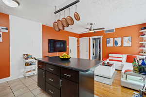 Kitchen featuring open floor plan, a textured ceiling, dark countertops, ceiling fan, and a kitchen island