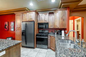 Kitchen with refrigerator with ice dispenser, black microwave, stainless steel range with gas cooktop, dark stone counters, and light tile patterned flooring
