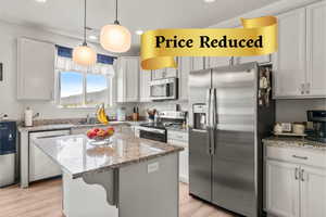 Kitchen with appliances with stainless steel finishes, a center island, light stone countertops, light wood-style flooring, and pendant lighting