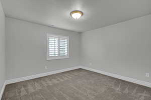 Carpeted spare room featuring a textured ceiling and baseboards