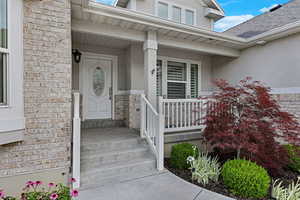 Entrance to property with stucco siding, covered porch, roof with shingles, and brick siding