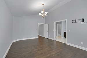 Empty room featuring a chandelier, high vaulted ceiling, and dark wood finished floors