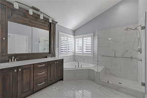 Full bath with vaulted ceiling, a bath, a marble finish shower, double vanity, and marble finish flooring