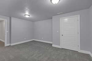 Empty room with a textured ceiling and dark carpet