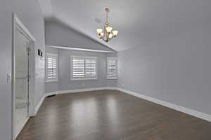 Spare room featuring vaulted ceiling, a chandelier, and dark wood-style floors