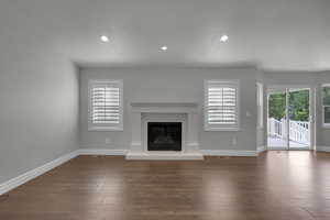 Unfurnished living room featuring a glass covered fireplace, recessed lighting, and dark wood-style flooring
