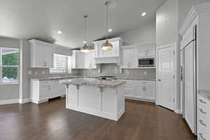 Kitchen with stainless steel microwave, tasteful backsplash, white cabinets, a kitchen island, and dark wood-type flooring